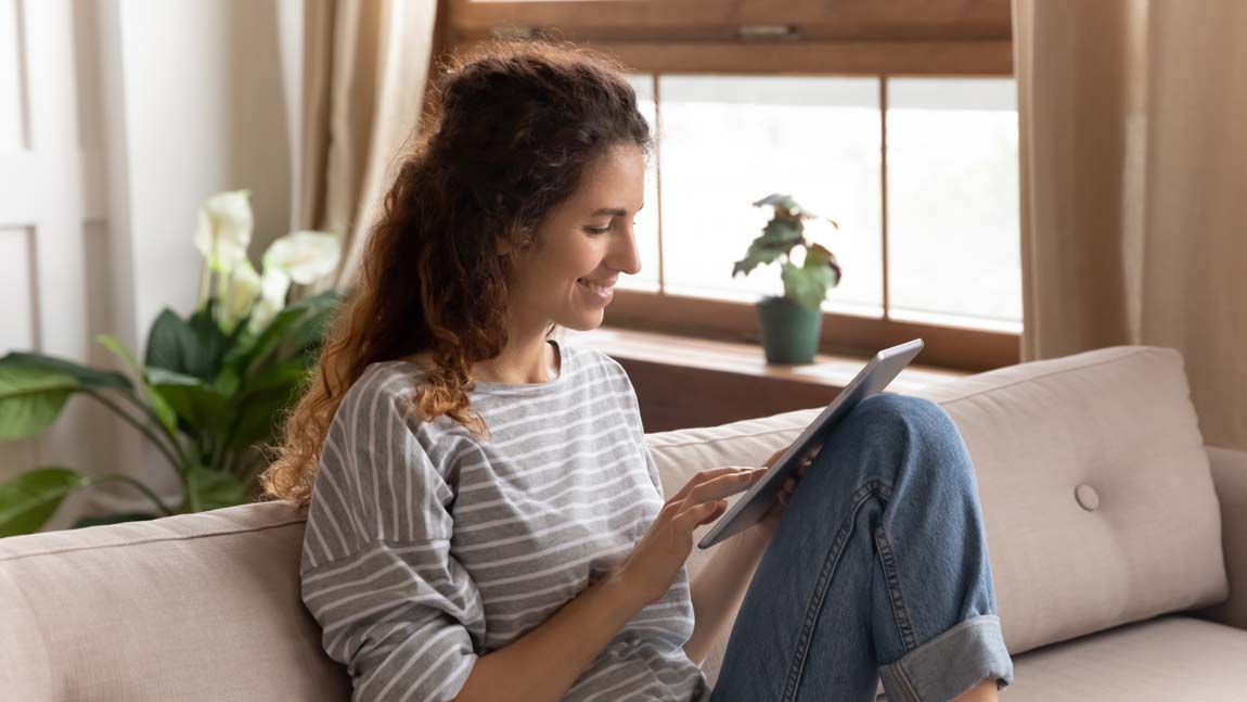 Tipps für die Familie digital lesen Eine junge Mutter sitzt auf der Couch und liest auf ihrem Tablet.