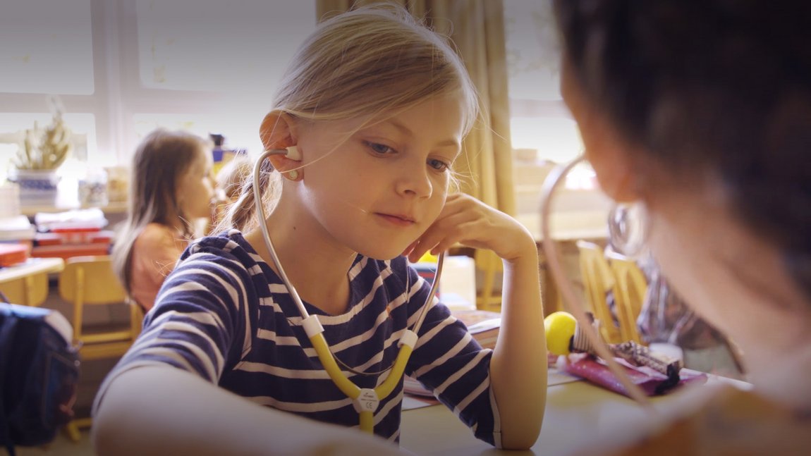 Kindergesundheit in Deutschland Mädchen sitzt im Klassenzimmer und hat ein Stethoskop in den Ohren