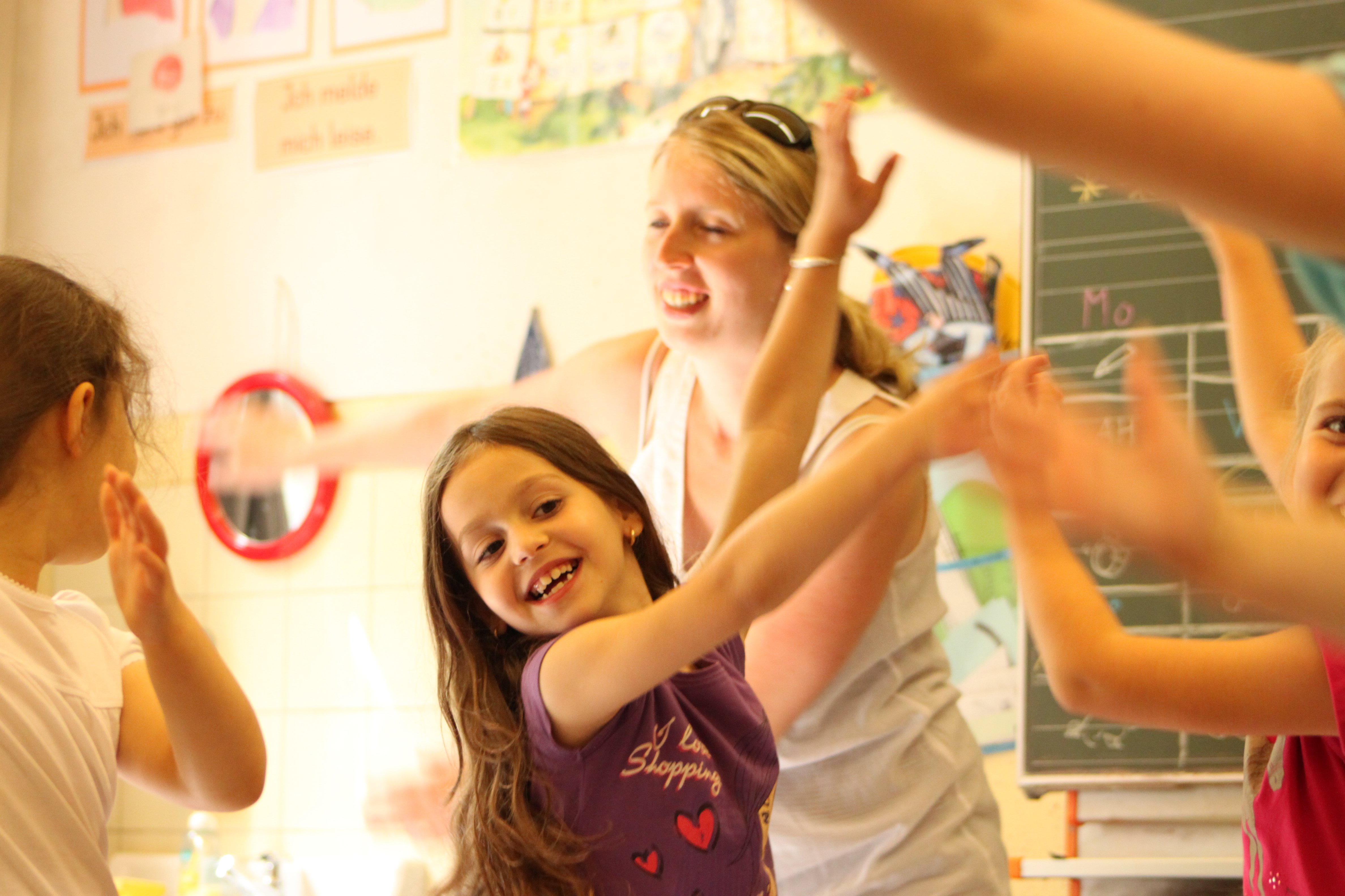Grundschulkinder schwingen mit der Lehrerin ihre Arme im Klassenzimmer 