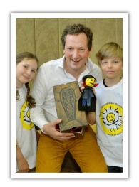 Eckart von Hirschhausen gratuliert zum 1. Millionsten Kind Eckart von Hirschhausen hält einen gebastelten Vampir KLARO in der Hand. Neben ihm stehen ein Mädchen und ein Junge mit weißem KLARO T-Shirt.