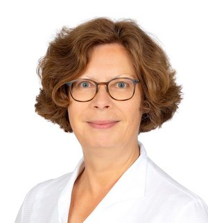 Dr. Caroline Bentgens Porträt vor weißem Hintergrund, von einer Frau mit dunklen, schulterlangen Haaren, Brille und weißer Bluse, die über ihre linke Schulter in die Kamera lächelt.
