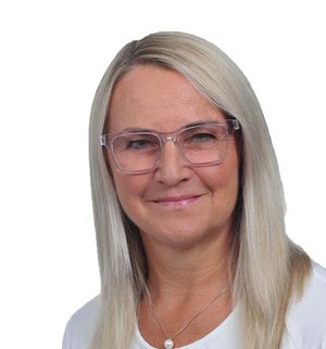 Ingrid Müller-Barth Porträt vor weißem Hintergrund, von einer Frau mit langen blonden Haaren, Brille und weißem T-Shirt, die in die Kamera lächelt.