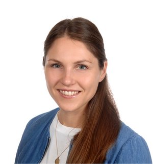Simone Gallus Porträt vor weißem Hintergrund, von einer Frau mit braunen langen Haaren und Pferdschwanz, bekleidet mit weißem T-Shirt und blauer Strickjacke, die über ihre linke Schulter in die Kamera lächelt.