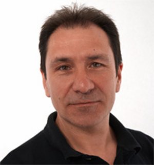 Winfried Amon Porträt eines dunkelhaarigen Manns mit schwarzem Poloshirt, der in die Kamera lächelt.