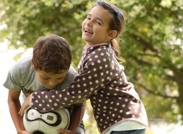 Draußen spielen macht Spaß In einem Garten versucht ein lachendes Mädchen ihrem lachenden Freund einen Fußball aus den Händen zu nehmen.