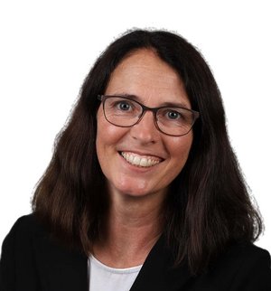 Marlott Wowerath Porträt vor weißem Hintergrund, von einer Frau mit schulterlangen braunen Haaren, Brille, weißem T-Shirt und schwarzem Blazer, die in die Kamera lächelt.