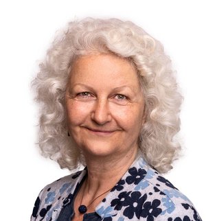 Regina Ohlwerter Porträt vor weißem Hintergrund, von einer Frau mit schulterlangen weißen gelockten Haaren, blau weiß geblümte Bluse und Kette, die über ihre linke Schulter in die Kamera lächelt.