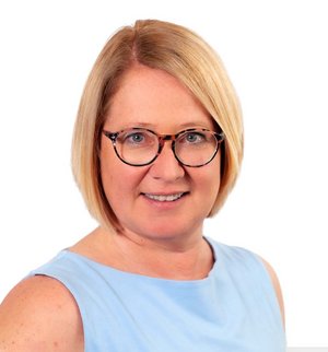 Ulrike Dreihäupl Porträt vor weißem Hintergrund, von einer Frau mit blonden, schulterlangen Haaren, Brille und hellblauer Bluse, die über ihre rechte Schulter in die Kamera lächelt.