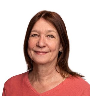 Gabriele Eibert Porträt vor weißem Hintergrund, von einer Frau mit braunen, langen Haaren und apricotfarbenem Strickpullover, die frontal in die Kamera lächelt.