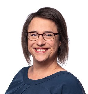 Lea Hack Porträt vor weißem Hintergrund, von einer Frau mit dunklen, schulterlangen Haaren, Brille und dunkelblauer Bluse, die über ihre linke Schulter in die Kamera lächelt.