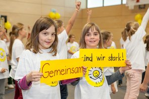 Zwei Mädchen in KLARO-T-Shirts halten je ein gelbes Plakat hoch. Dort steht "Gemeinsam sind wir stark".