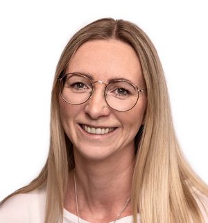 Andrea Meyer Porträt vor weißem Hintergrund, von einer Frau mit langen blonden Haaren, Brille und weißem T-Shirt, die in die Kamera lächelt.