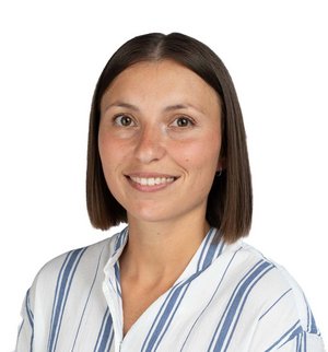 Janina Luickx Porträt vor weißem Hintergrund, von einer Frau mit kurzen braunen Haaren, weiß blau gestreifter Bluse, die über ihre linke Schulter in die Kamera lächelt.