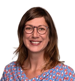 Rebekka Frey Porträt vor weißem Hintergrund, von einer Frau mit braunen, langen Haaren, Brille und blau gemustertem Shirt, die frontal in die Kamera lächelt.